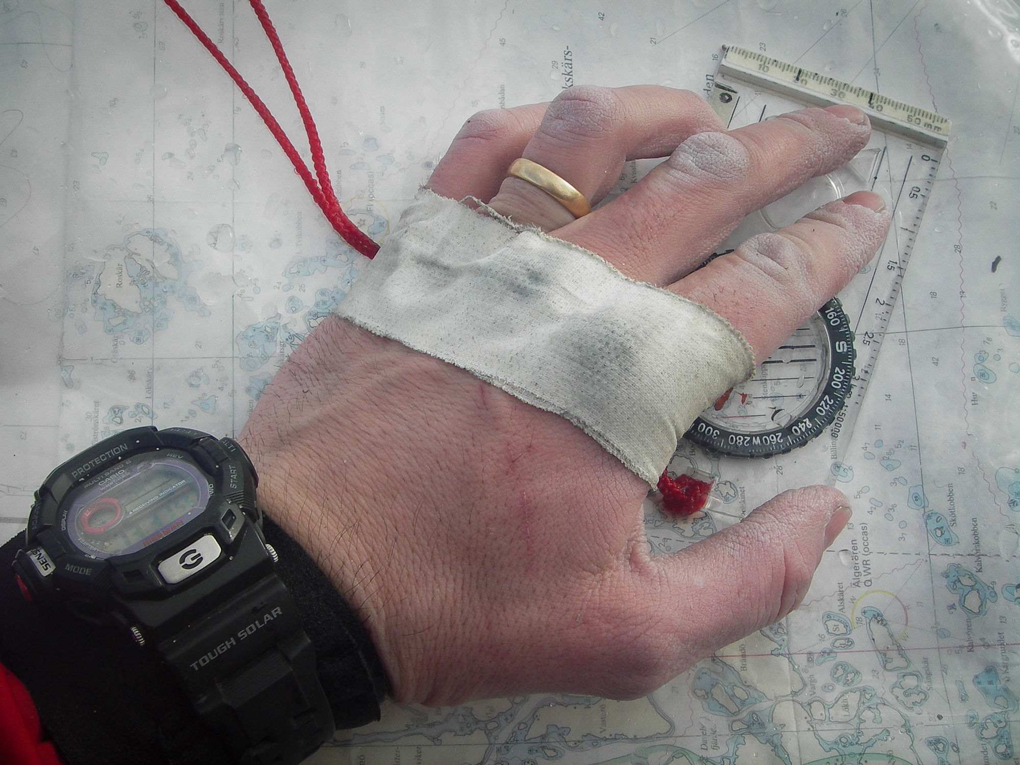 Skavsårstejpad hand håller en kompass mot ett sjökort.
