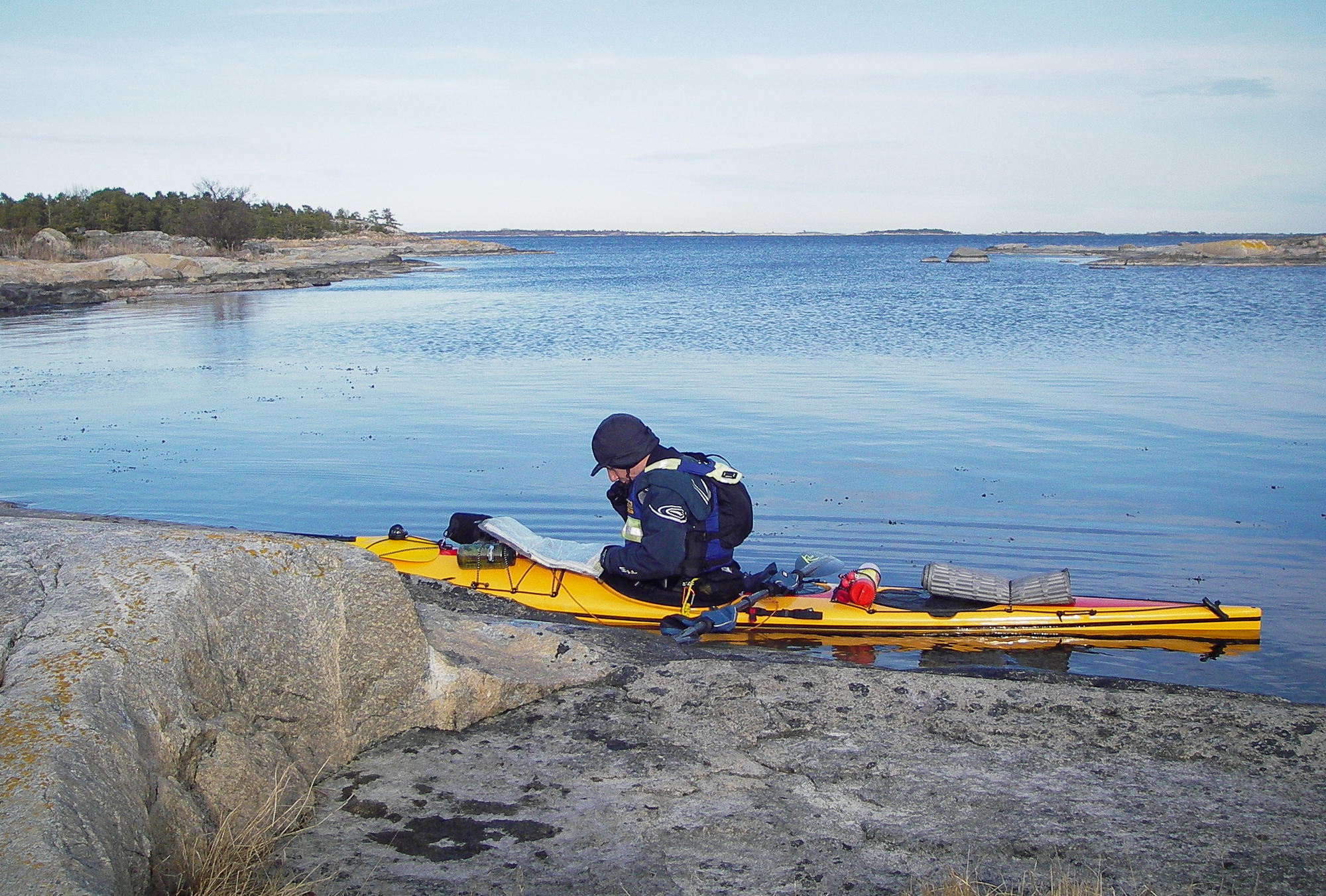 Havskajakpaddlare studerar kartan vid en låg klippa i Stockholms skärgård.