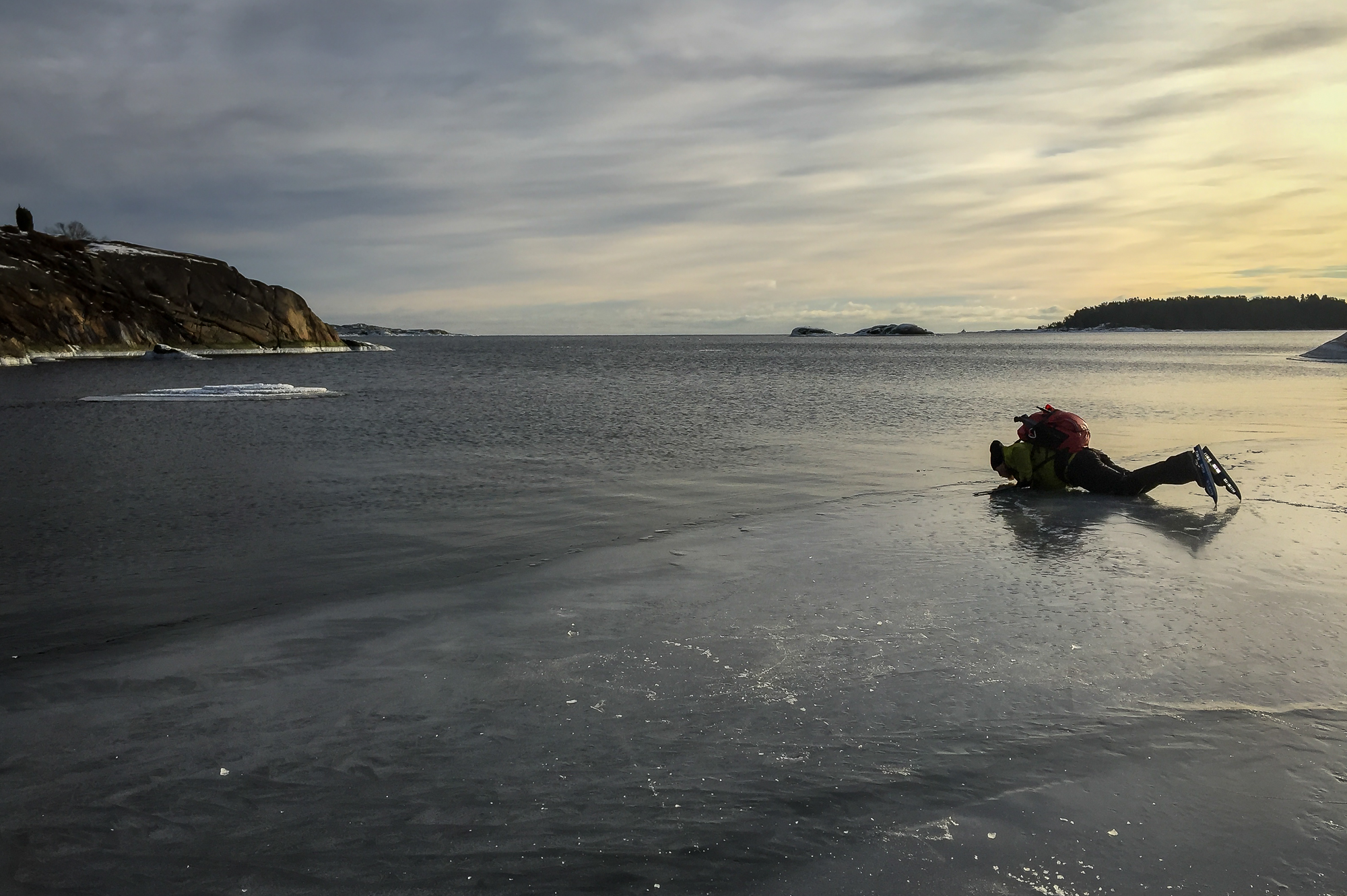 Långfärdsskridskoåkare ligger på mage intill iskant och provsmakar vattnet.