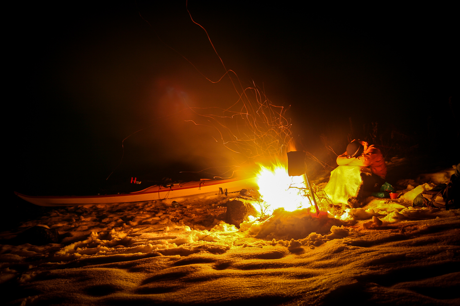 Kajakpaddlare värmer sig vid en lägereld i vinternatten i Stockholms skärgård.