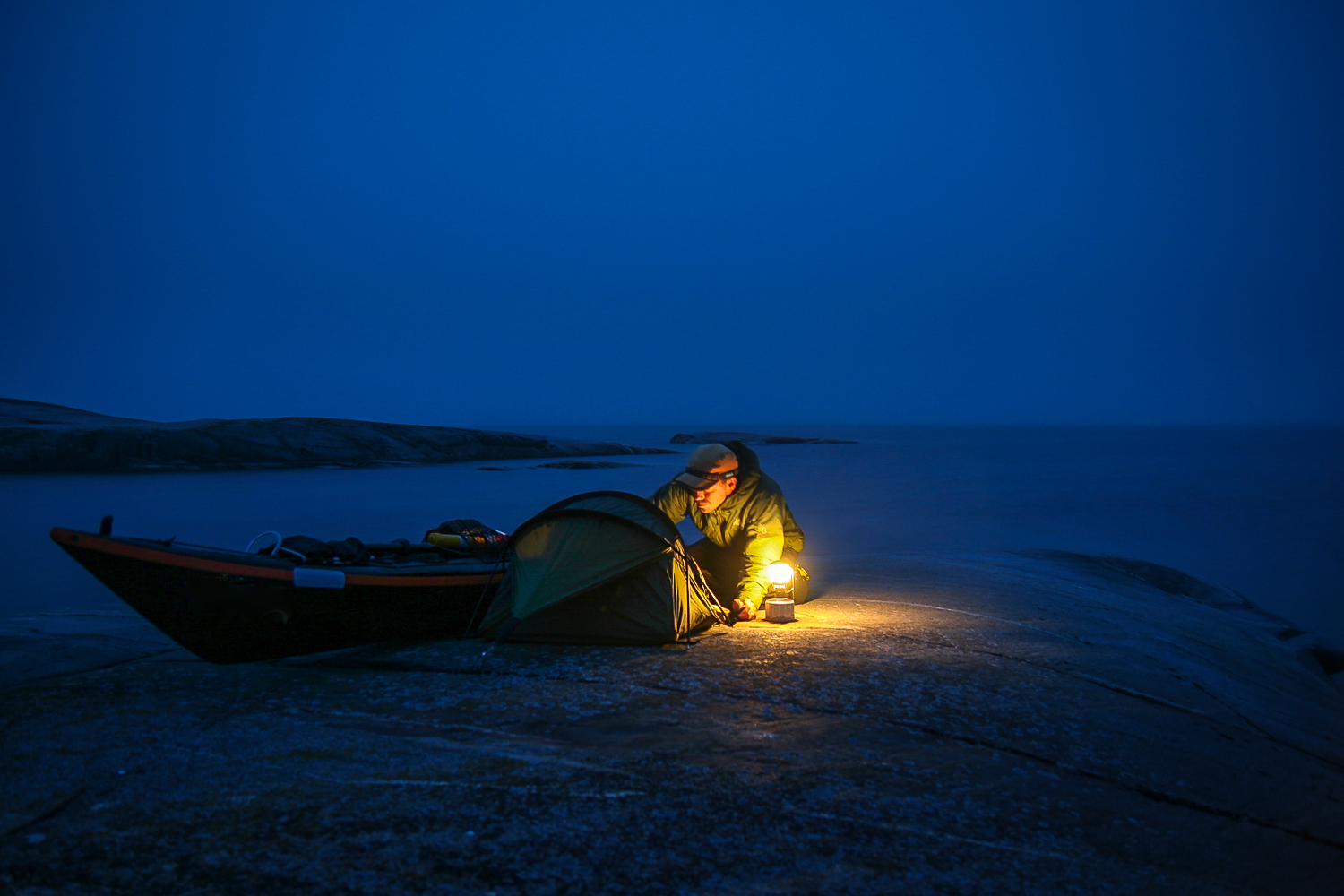 A man is preparing a divvy bag next to a sea kayak on a cliff close to the water