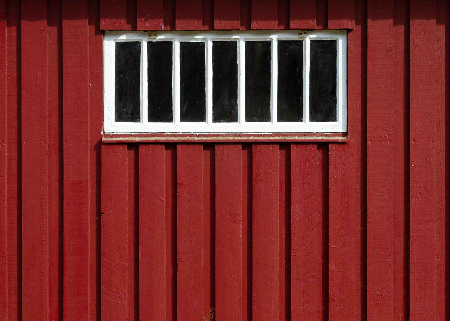 Ett vitt spröjsat fönster på en faluröd träpanelsvägg