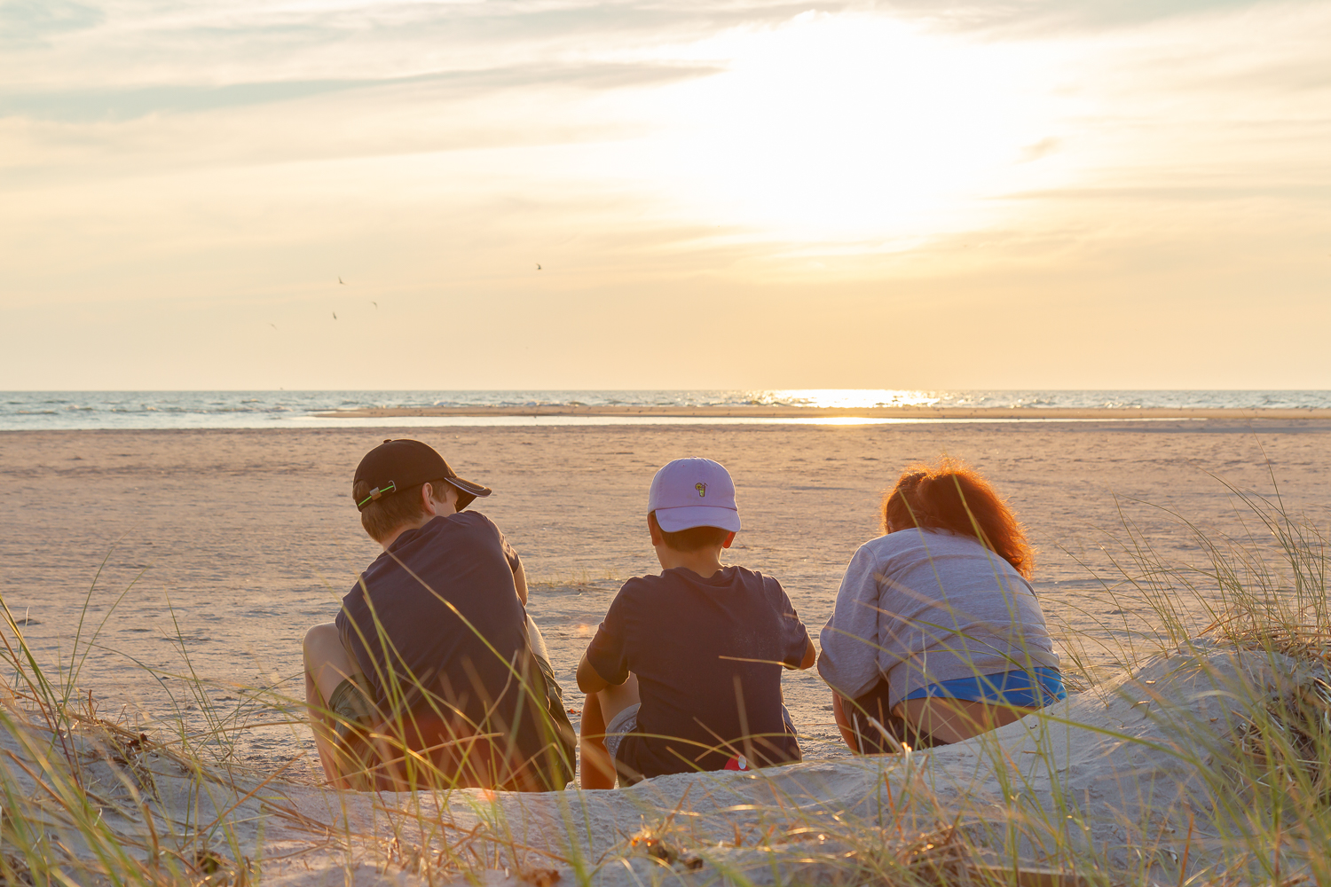 Tre personer sitter och njuter av solnedgången över Bredsandsudde, Gotska Sandön