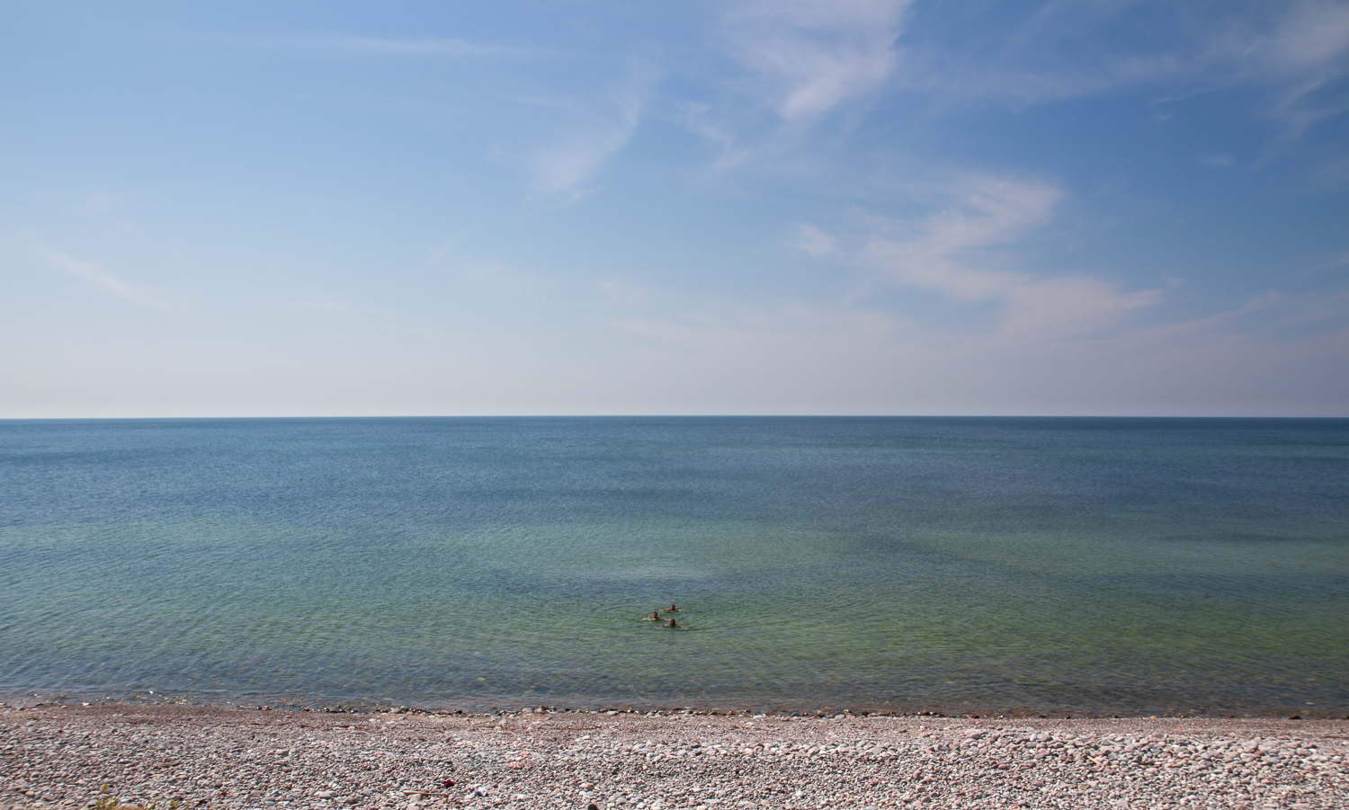 Tre personer badar i havet vid stenstranden Varvsbukten på Gotska Sandön