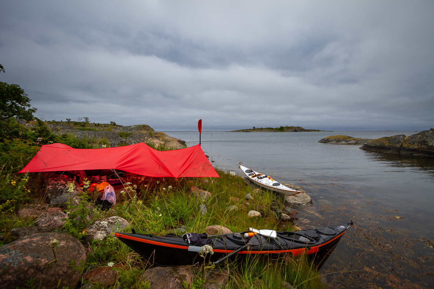 Kajakpaddlare lunchar under tarp i skydd från regnet i Ängskärs skärgård, Stockholms skärgård