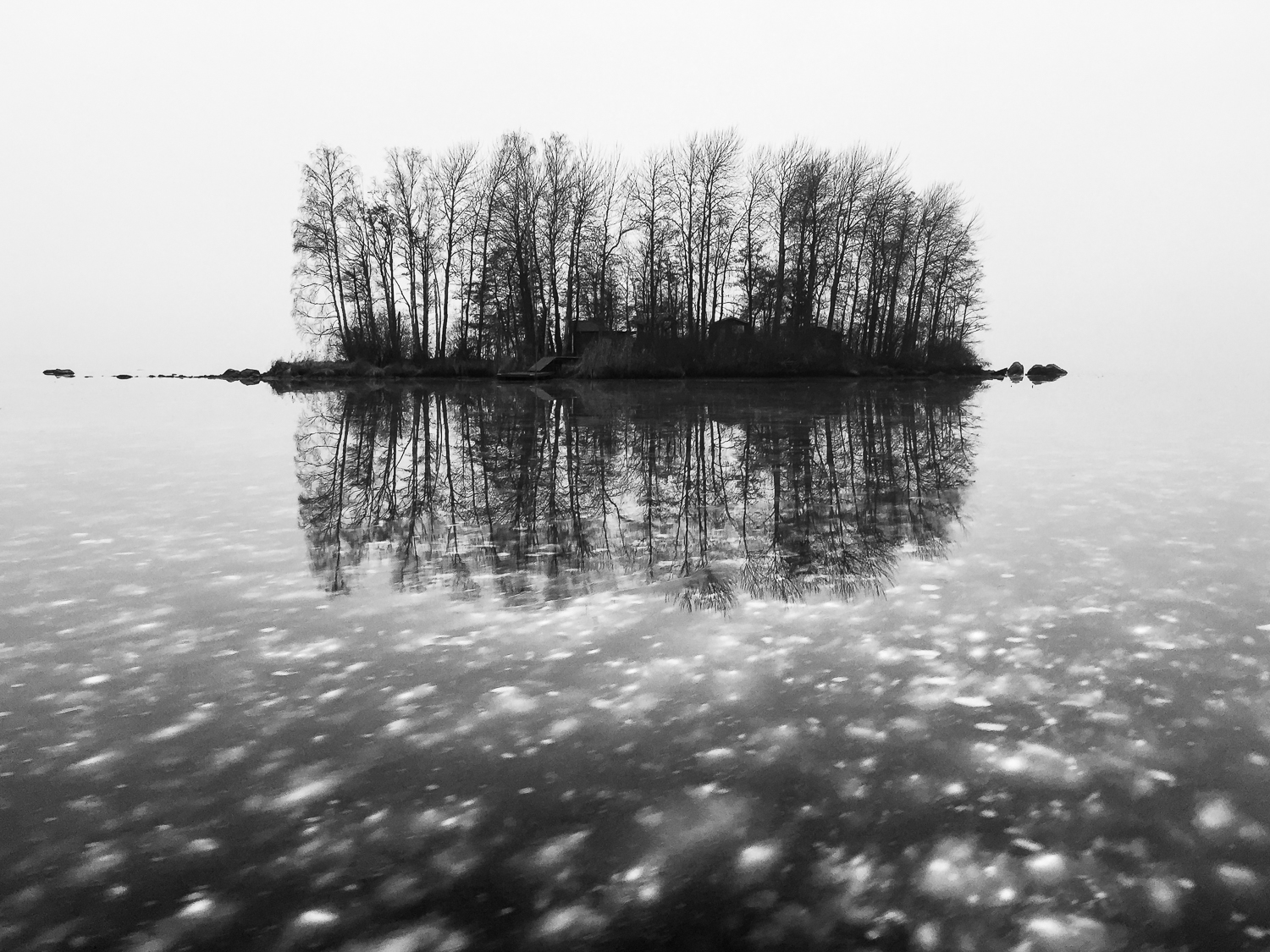 Enslig ö speglar sig i blank kärnis med infrusna snöfläckar