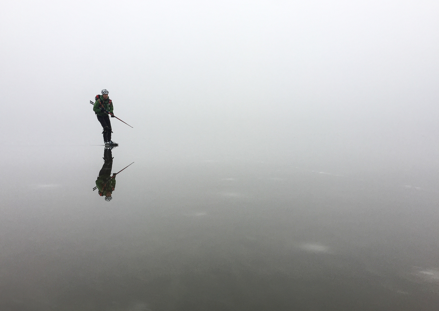 Långfärdsskridskoåkare i dimma speglas i blank kärnis