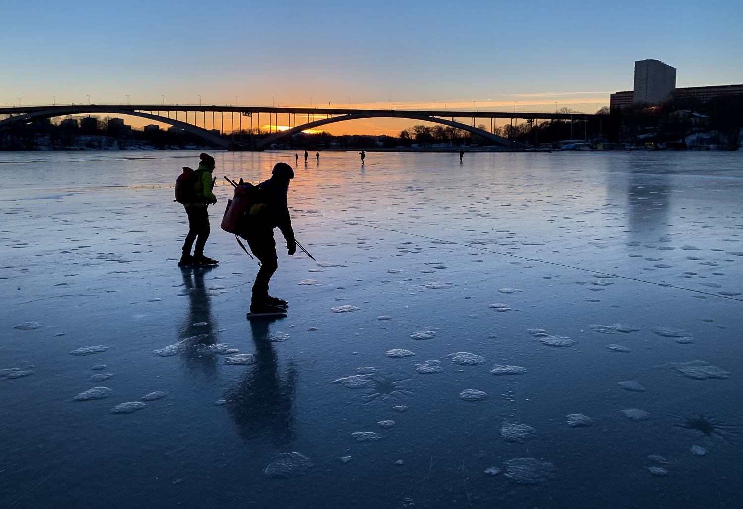 Långfärdsskridskoåkare på blankis i skymningen på Riddarfjärden med Västerbron i bakgrunden, Stockholm city