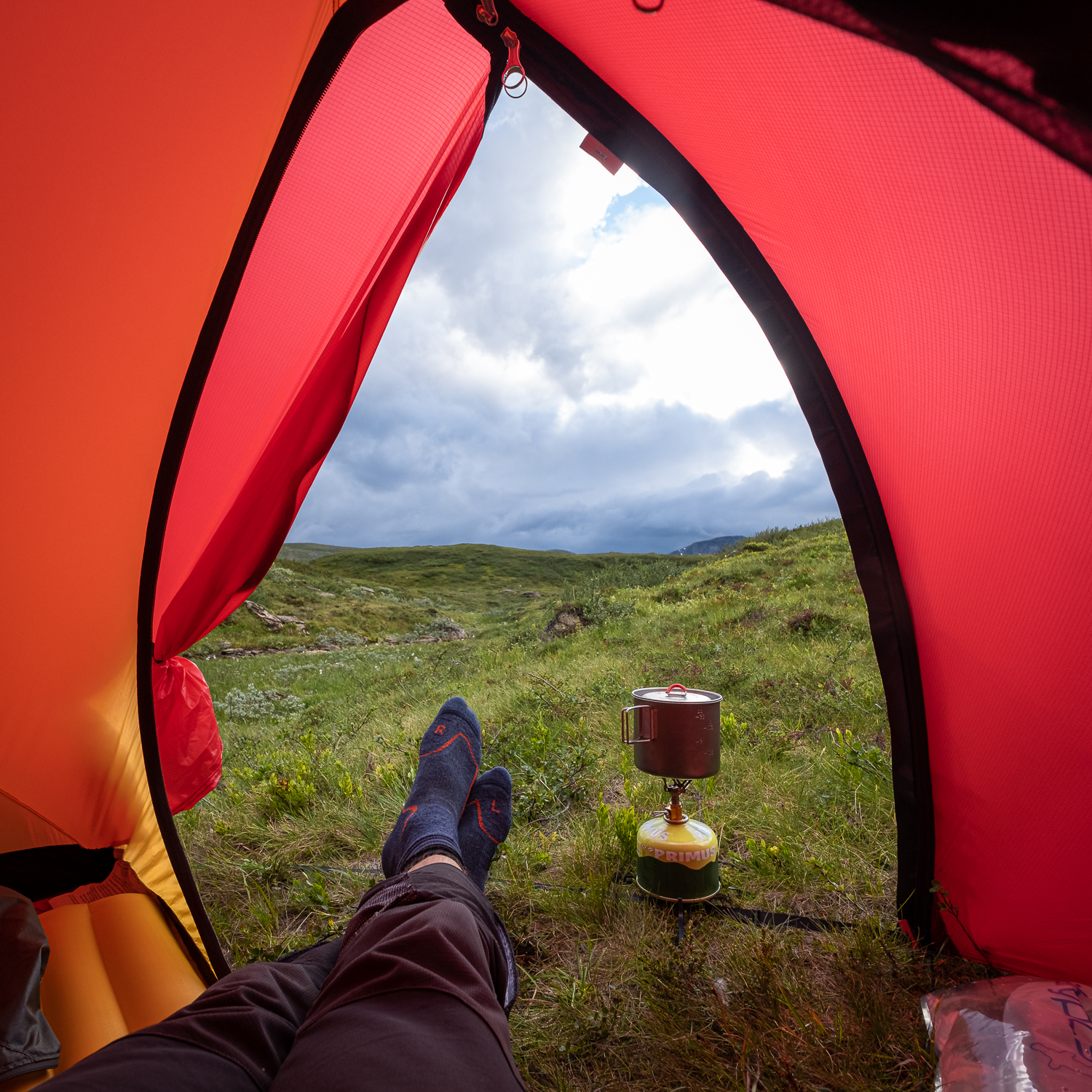 En fjällvandrare lagar mat på gaskök i tältet med utsikt över Jämtlandsfjällen
