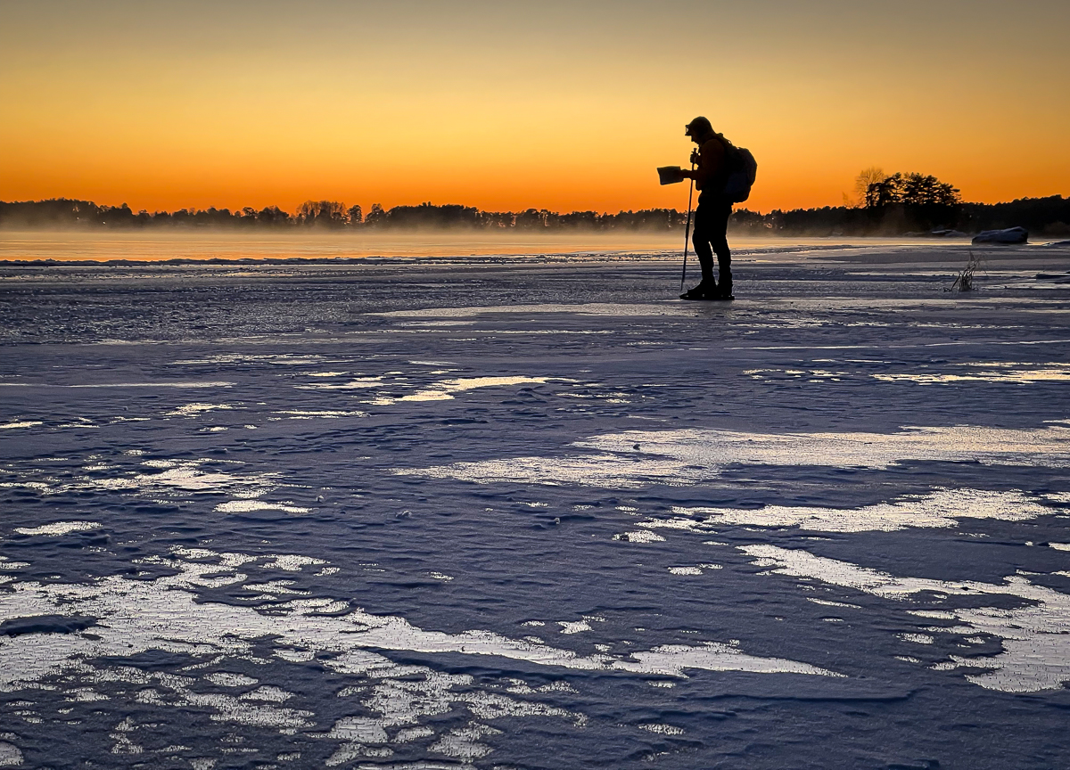 Långfärdsskridskoåkare i solnedgång och sjörök vid strömfåran Gnupe, Dalälven.